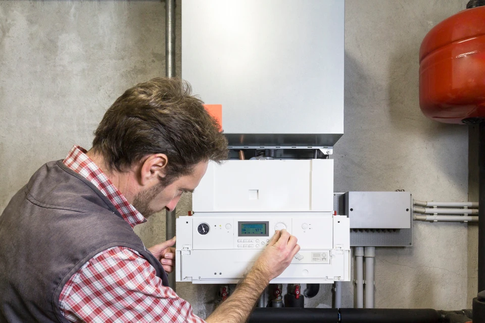 Technicien en combinaison de travail effectuant la maintenance d'une chaudière murale dans une chaufferie domestique