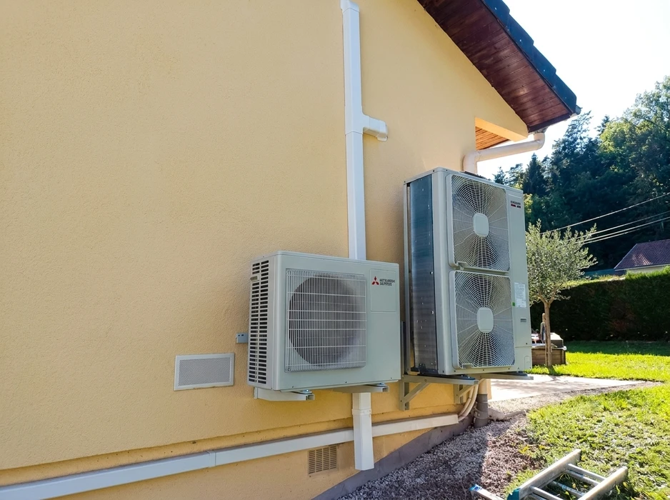 Installation extérieure de climatisation sur façade enduite jaune d'une maison