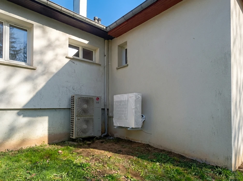 Angle extérieur d'une maison avec deux unités extérieures de climatisation/pompe à chaleur installées contre un mur en enduit blanc