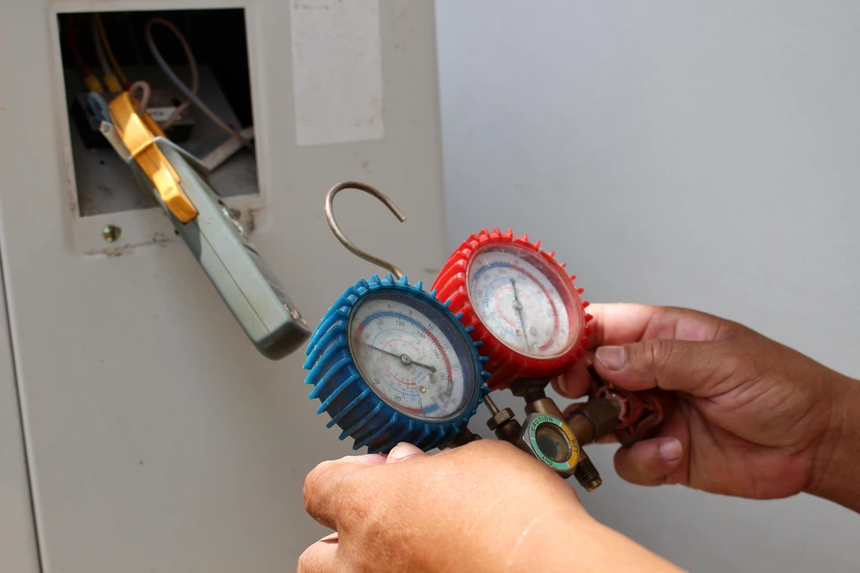 Technicien en climatisation travaillant sur une unité extérieure de pompe à chaleur devant un bâtiment moderne à bardage bois